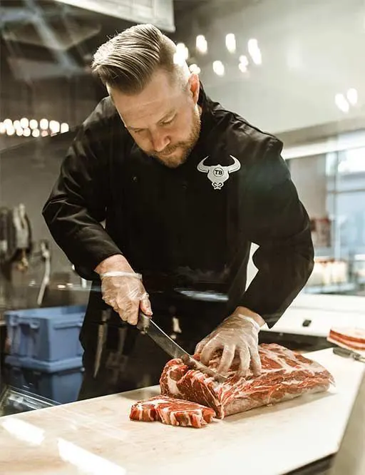 Le Manager de la Boucherie, Michel Ducas préparant avec précision des pièces de viande d'exception pour la carte gastronomique du restaurant La Cigogne Itinérante à Kaysersberg.